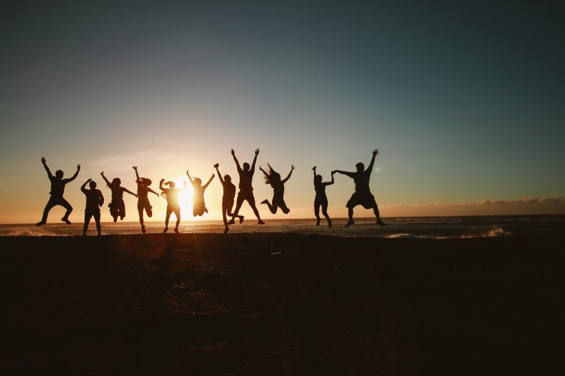 Image of shadows of 11 people jumping in the air with the beach at sunset as a background
